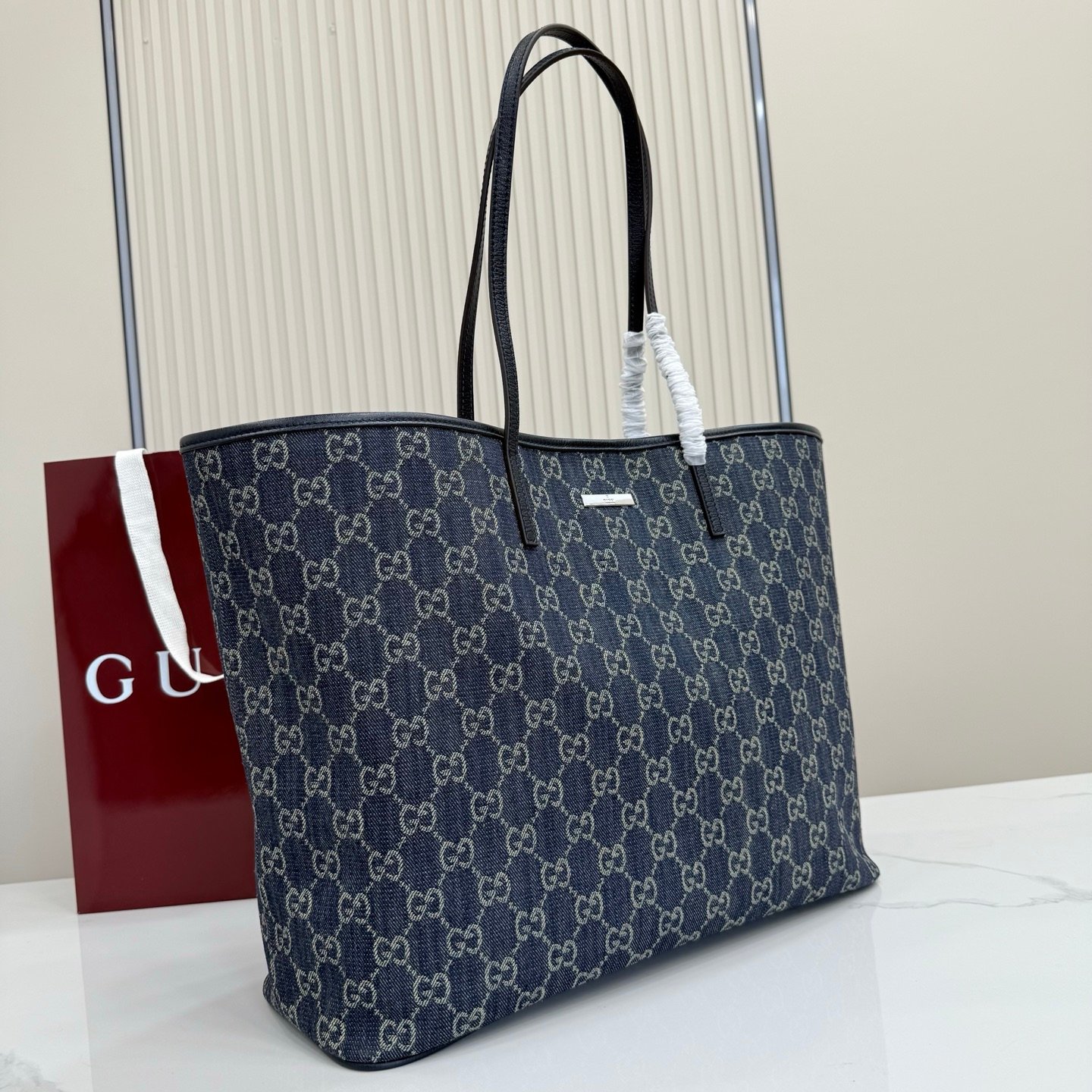 将不同世代的设计融入一个美学叙事中。GG牛仔布搭配品牌标识徽牌，为精致廓形增添标志性细节。这款托特包提升了日常风格，内部配有拉链口袋。