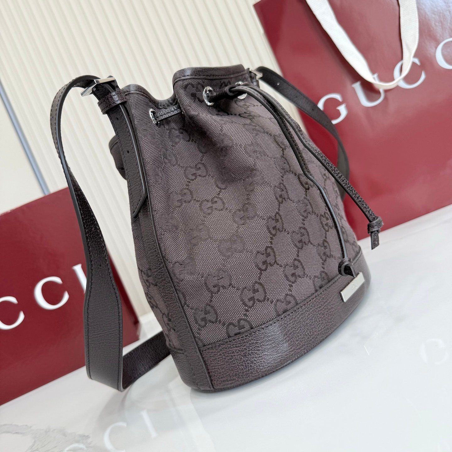 Generation Gucci系列深入探索品牌的典藏元素，将不同世代的设计融合成一种美学叙事。GG深棕色帆布为多功能小型皮具带来品牌标志性的点缀，比如这款设计用于存放日常必需品的水桶包。