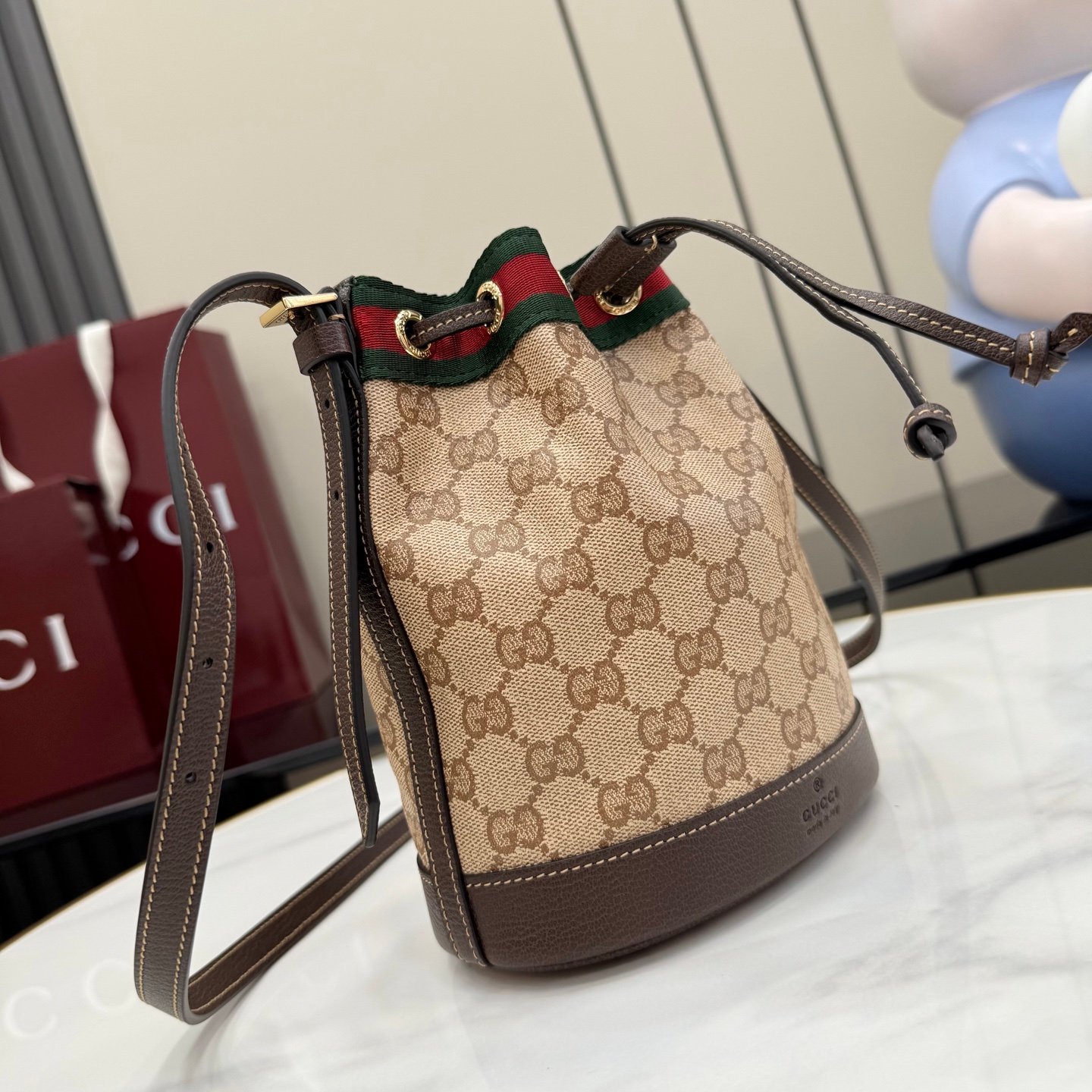 配全套原厂专柜包装 Generation Gucci古驰世代系列深入探索品牌的典藏元素，将不同世代的设计融合为统一的美学叙事。GG涂层帆布搭配经典织带，为多功能小型皮具带来标志性风格，如这款设计用于存放日常必需品的水桶包。