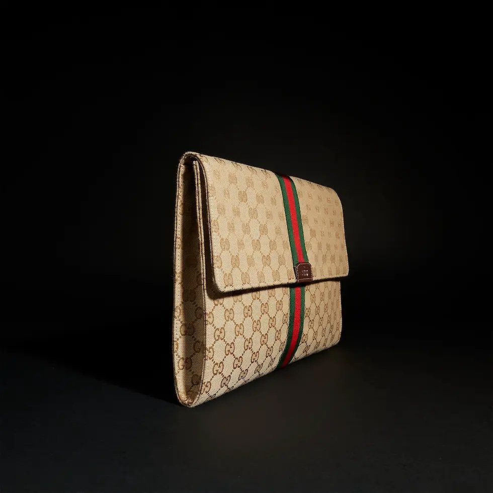 Generation Gucci系列深入探索品牌的典藏元素，将不同世代的设计融合成一种美学叙事。这款手拿包采用GG帆布制作，并饰有织带，是公文包的理想替代品。