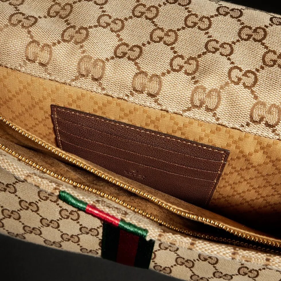 Generation Gucci系列深入探索品牌的典藏元素，将不同世代的设计融合成一种美学叙事。这款手拿包采用GG帆布制作，并饰有织带，是公文包的理想替代品。