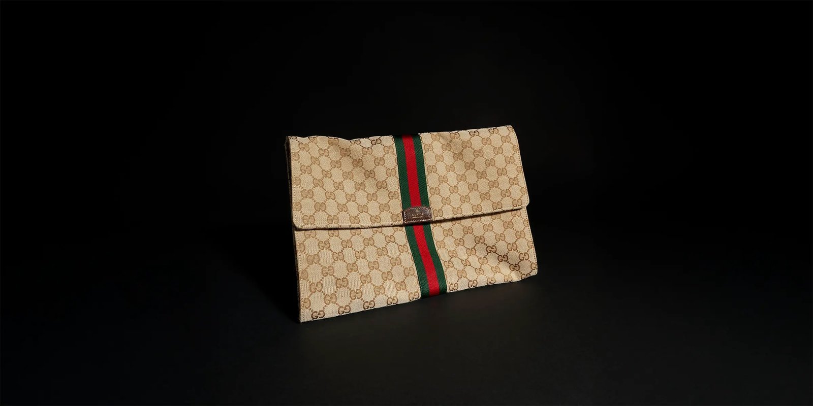 Generation Gucci系列深入探索品牌的典藏元素，将不同世代的设计融合成一种美学叙事。这款手拿包采用GG帆布制作，并饰有织带，是公文包的理想替代品。