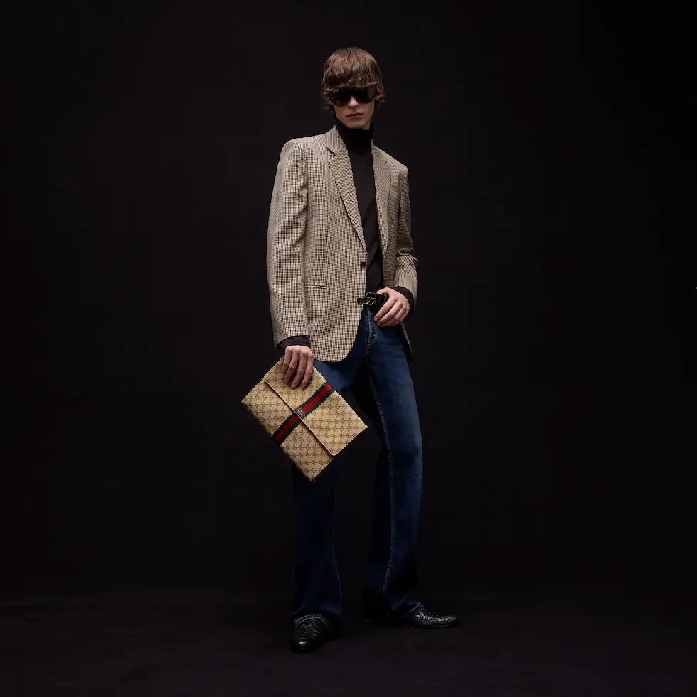 Generation Gucci系列深入探索品牌的典藏元素，将不同世代的设计融合成一种美学叙事。这款手拿包采用GG帆布制作，并饰有织带，是公文包的理想替代品。