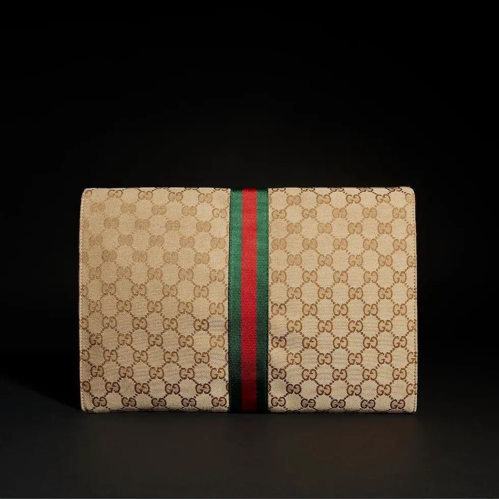 Generation Gucci系列深入探索品牌的典藏元素，将不同世代的设计融合成一种美学叙事。这款手拿包采用GG帆布制作，并饰有织带，是公文包的理想替代品。