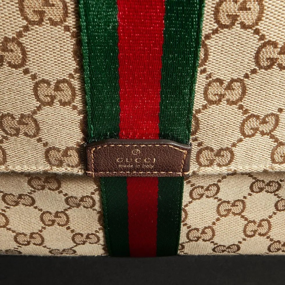 Generation Gucci系列深入探索品牌的典藏元素，将不同世代的设计融合成一种美学叙事。这款手拿包采用GG帆布制作，并饰有织带，是公文包的理想替代品。